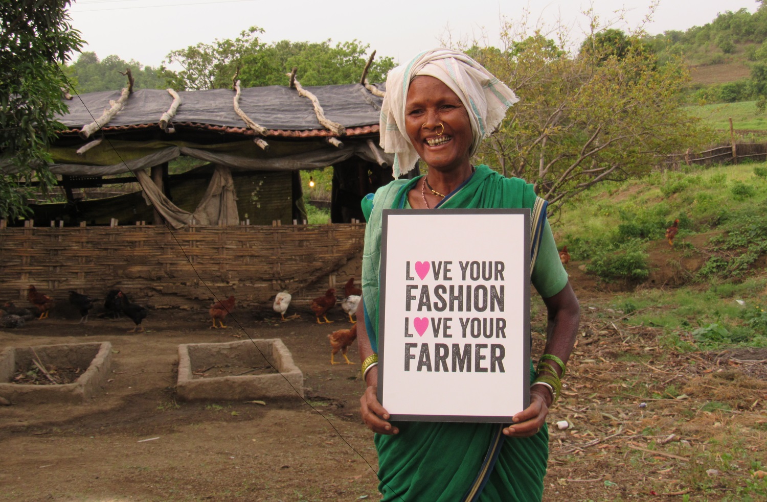 Lingu Bai, a Fairtrade cotton farmer with Chetna Organic in the Adilabad District, India, holding a sign that says, "Love your fashion, love your farmer"