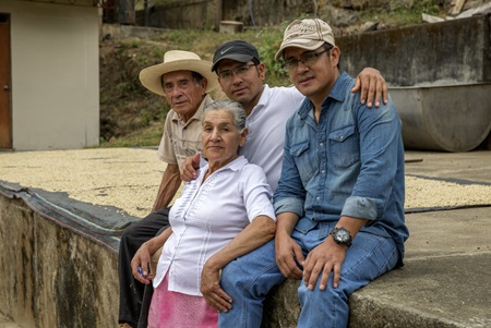 Coffee farmer Hugo Guerrero sits with family beside drying coffee beans
