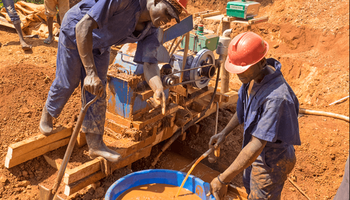 Miners wearing helmets, work the ore crushing machine and pan and wash for specks of gold at the Tiira mine.