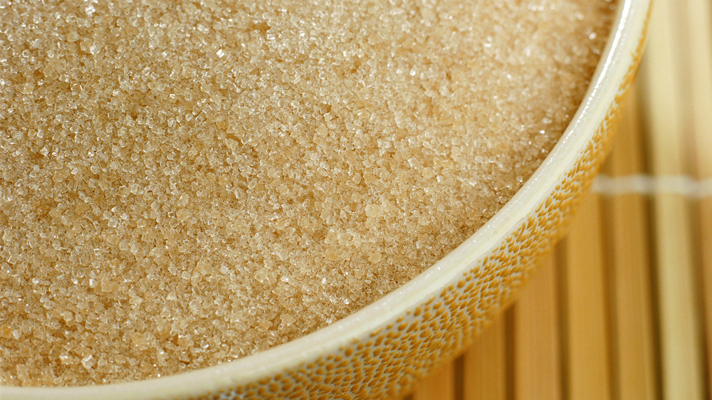 Sugar grains in yellow bowl on wood slat mat