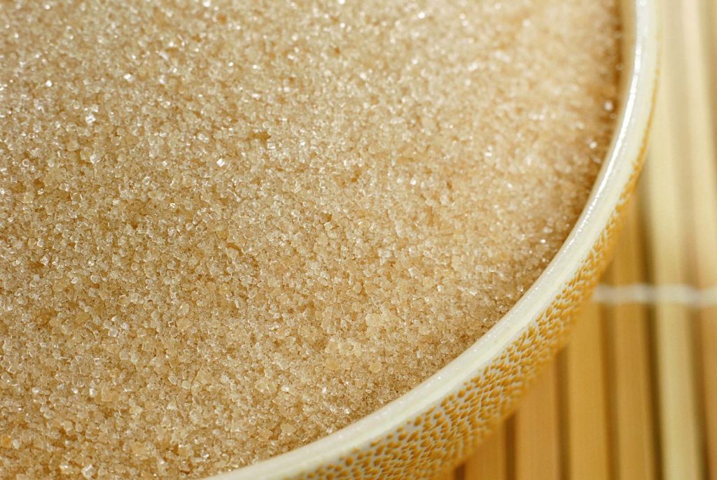 Sugar grains in yellow bowl on wooden slat mat