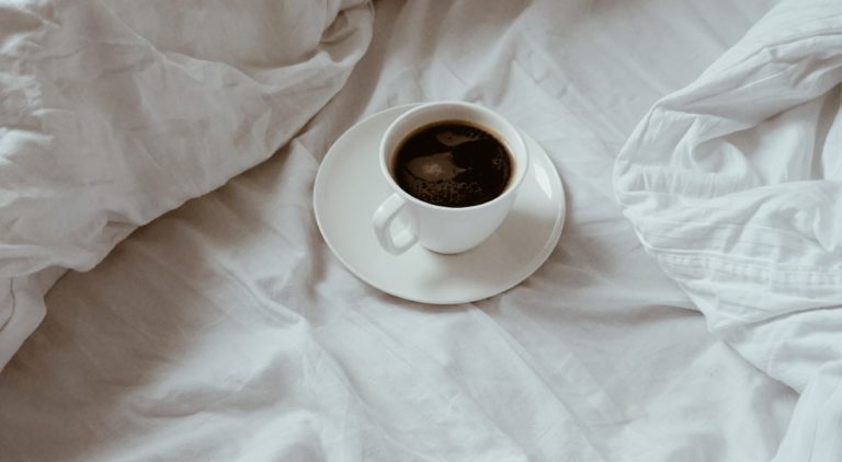Cup of black coffee on white duvet