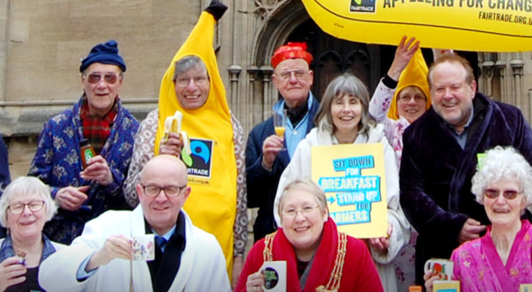 Fairtrade campaigners, dressed in pajamas and dressing gowns, and banana suits, drinking from Fairtrade mugs at a Fairtrade fundraising event in front of a church