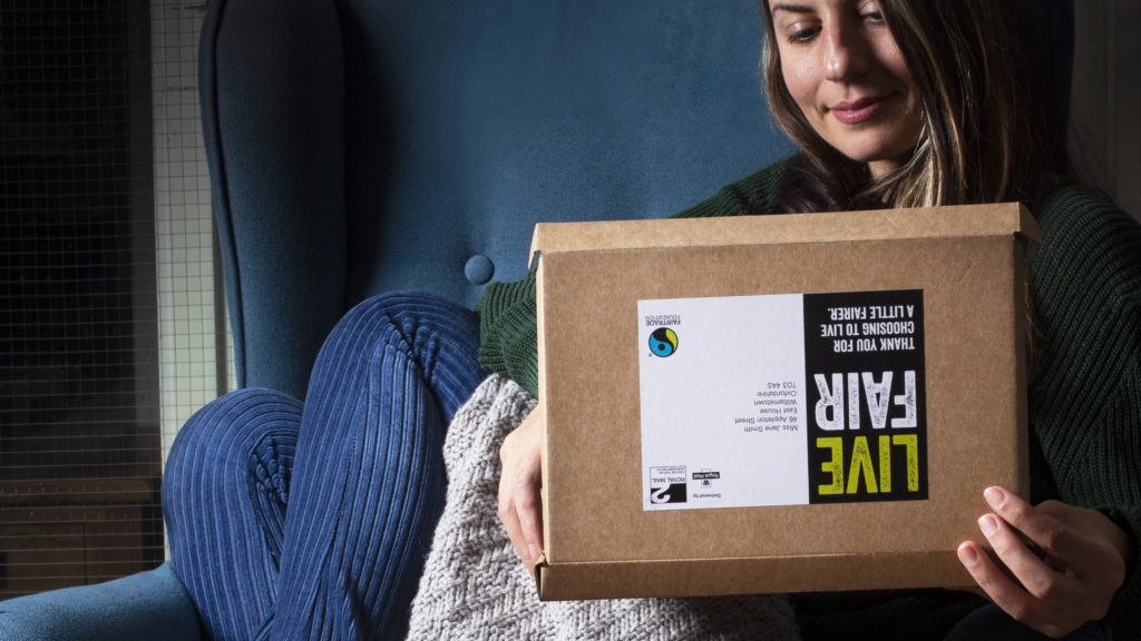 A woman on a comfy settee looks inside the Live Fair Fairtrade box