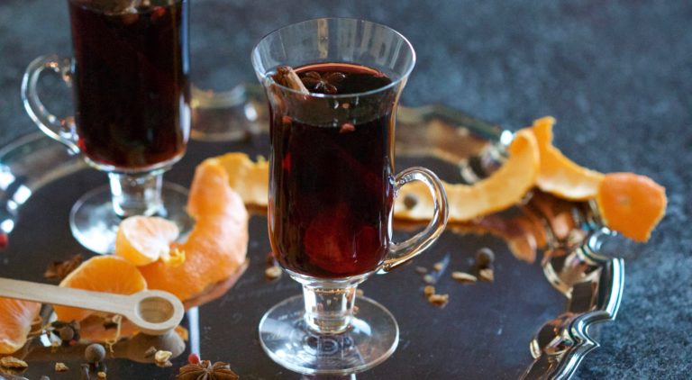 Asthetic picture of mulled wine in a glass with spices and orange peel scattered around it