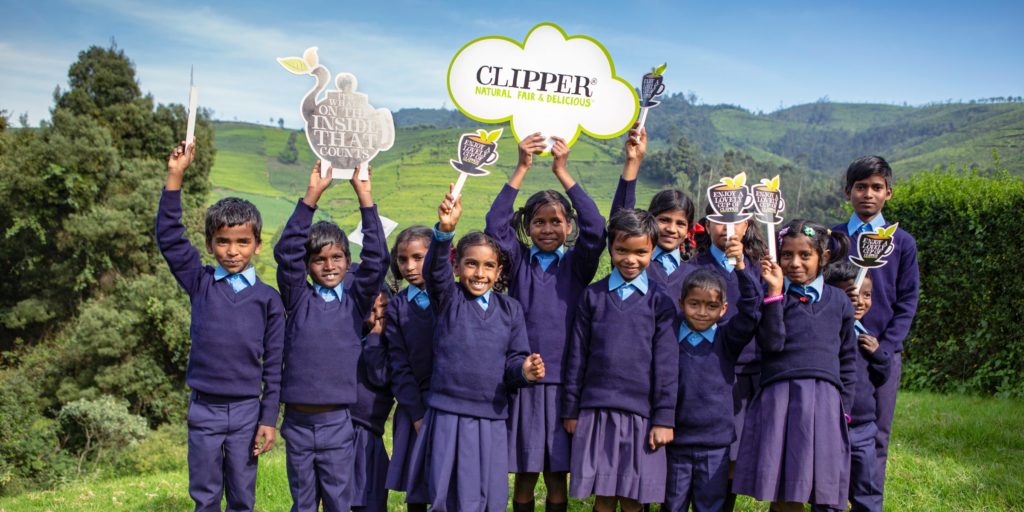 School children in a field in India holding up Clipper branded images of teapots and tea cups