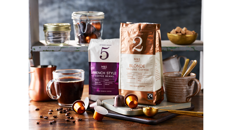 M&S coffee in a glass, capsule and packs of coffee on wooden tabletop with a grey wall background