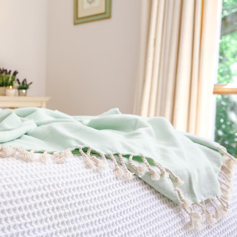 Organic Brushed Cotton Herringbone Throw - Aqua - presented on a white bed cover in a white painted room with a view of foliage from the window