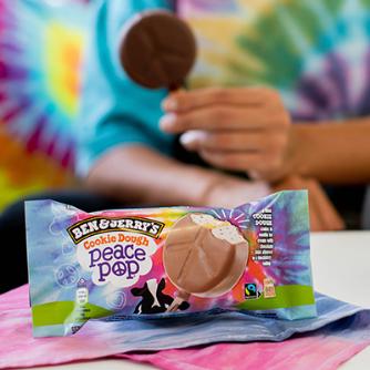 Ben & Jerry's Cookie Dough Peace Pop in foreground. Someone holding the peace pop wearing a tie dye t-shirt in the background