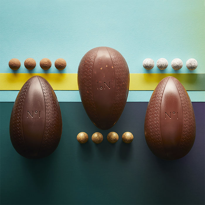 Three chocolate eggs with four truffles aligned at the top of each egg. Striped background