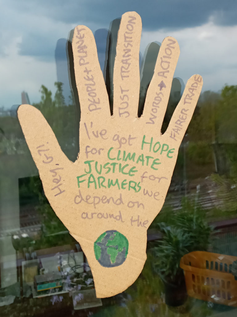 Cardboard hand with message 'I've got hope for climate justice for farmers we depend on around the (picture of the world)' stuck to window