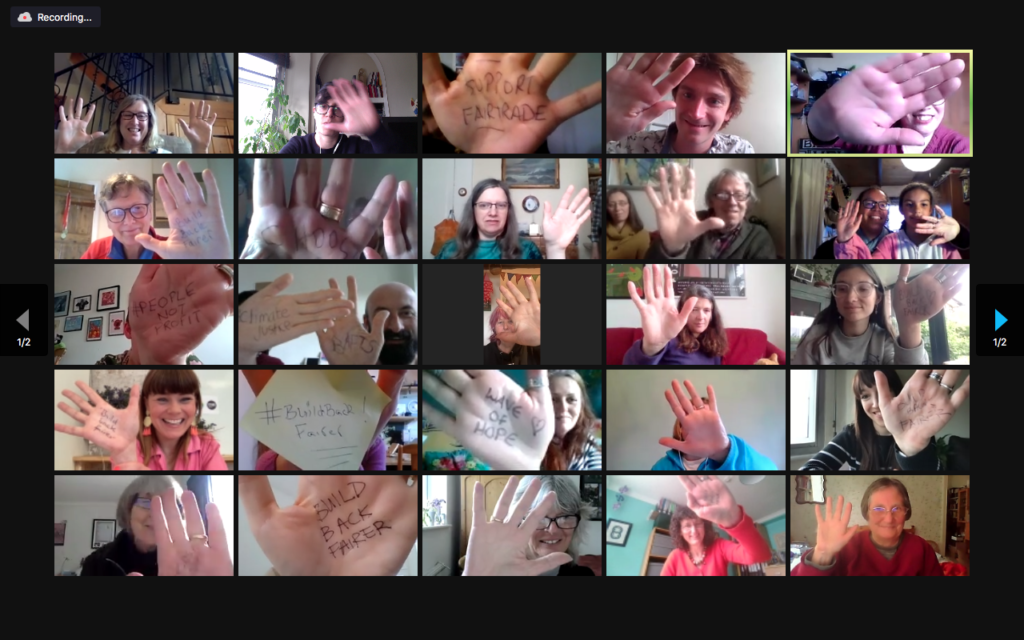 15 people on a zoom gallery, holding up their hands, with messages written on some of their palms - messages 'Build Back Fairer,' 'Wave of Hope.'