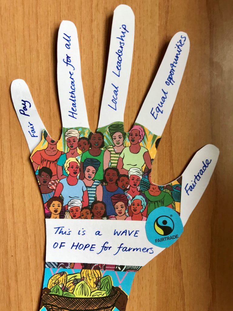 Homemade cut out paper hand, with colourful illustration of cocoa farmers and across the palm a message, 'This is a wave of hope for farmers.'