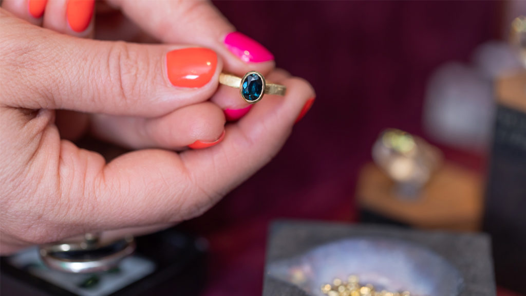 Zoe de Pass holding a Fairtrade gold ring, gold nuggets at the bottom of the photo