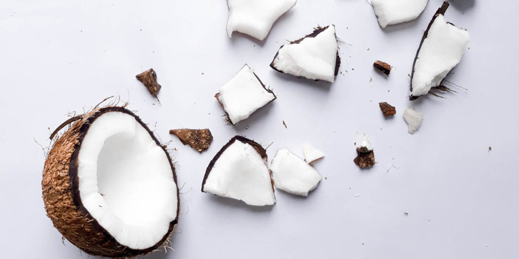 Coconut half with chunks of coconut artfully scattered on a white background