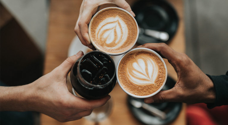 three hands holding cups of coffee together over a table