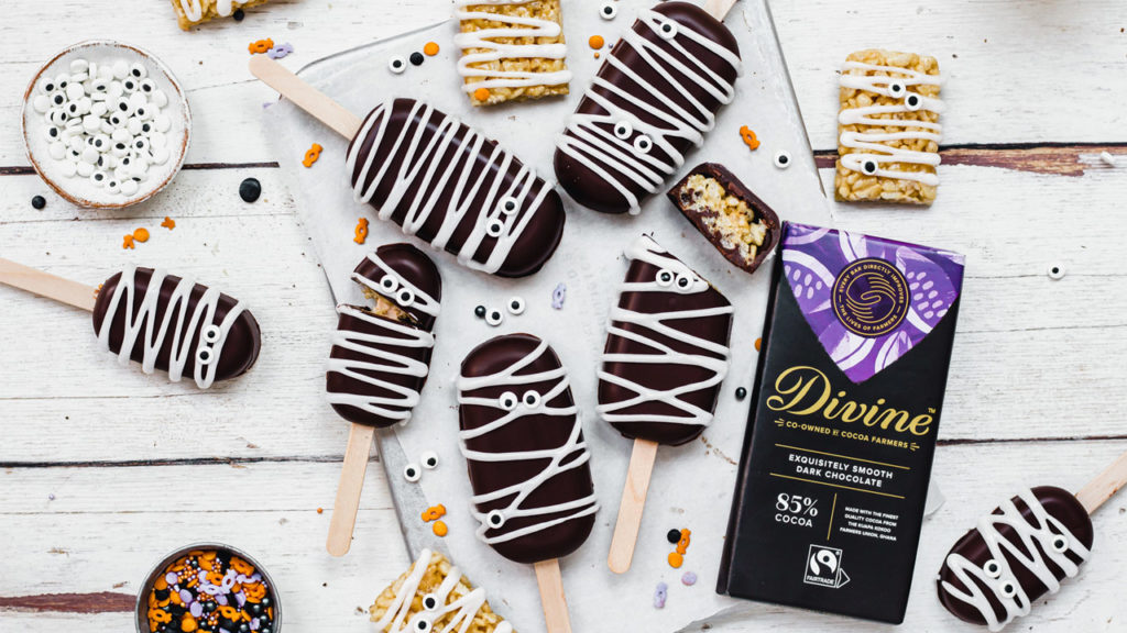 Spooky mummy rice crispy pops on a table with icing eye decorations and a bar of Divine 85% dark chocolate