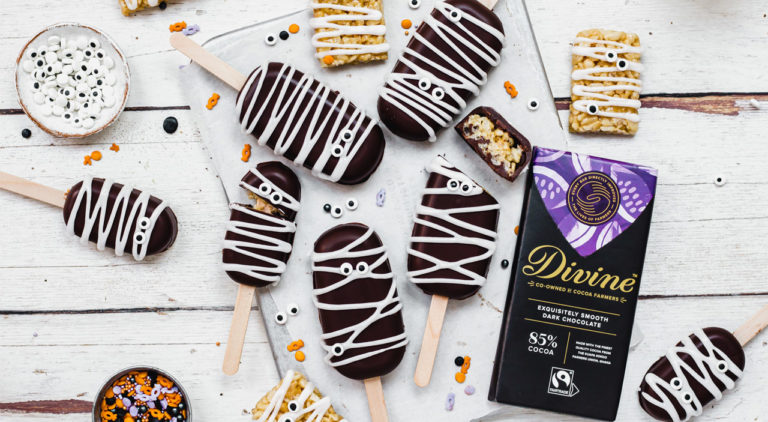 Spooky mummy rice crispy pops on a table with icing eye decorations and a bar of Divine 85% dark chocolate
