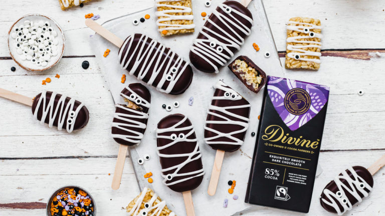 Spooky mummy rice crispy pops on a table with icing eye decorations and a bar of Divine 85% dark chocolate