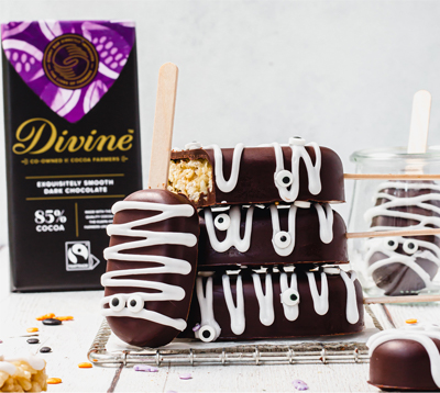 Spooky mummy rice crispy pops on a table with icing eye decorations and a bar of Divine 85% dark chocolate