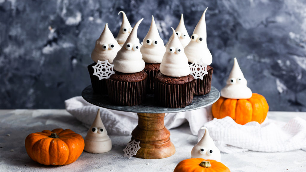 ghost meringue chocolate cupcakes on a cake stand, with snowflakes and miniature pumpkins as decoration