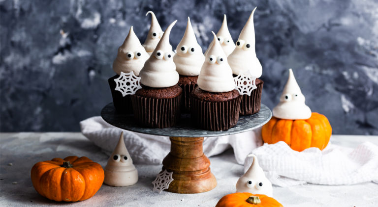 ghost meringue chocolate cupcakes on a cake stand, with snowflakes and miniature pumpkins as decoration