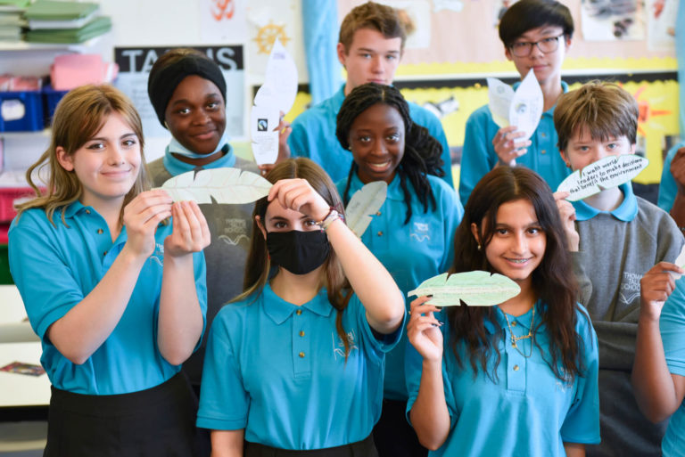 A group of young people holding up hand-written messages displayed on hand-crafted banana leaves, cocoa leaves, and coffee leaves, calling attention to the farmers who are most affected by the climate crisis.