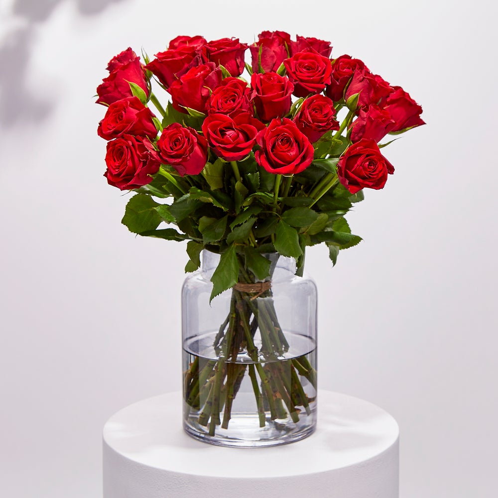 A glass vase of a dozen Arena Fairtrade Sweetheart red roses