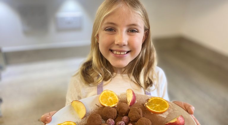 Young girl holding a plate of SuperPower Balls with orange and apple slices and raspberries