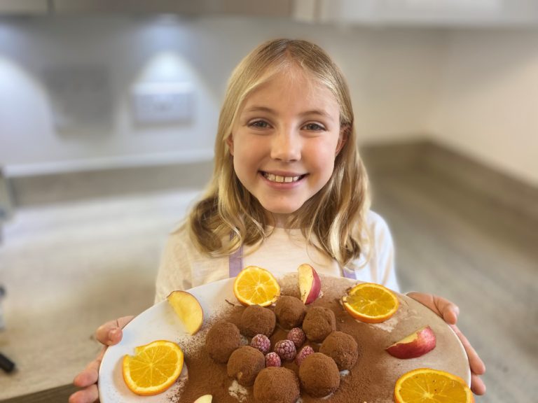 Young girl holding a plate of SuperPower Balls with orange and apple slices and raspberries
