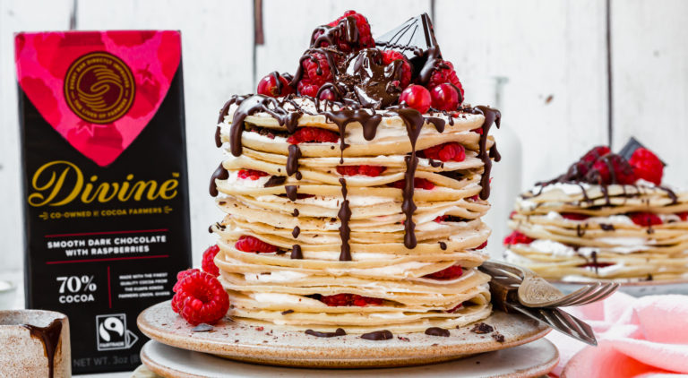 A stack of pancakes filled with cream and fruit with chocolate dripping from the top