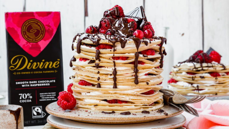 A stack of pancakes filled with cream and fruit with chocolate dripping from the top