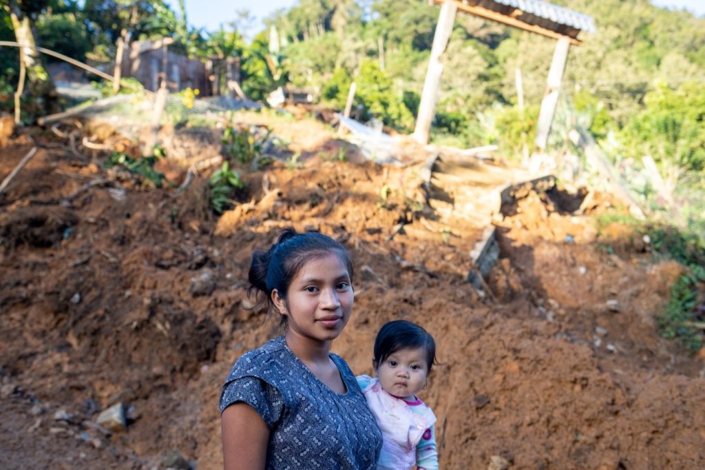 16 year old Lourdes López Vásquez_holding her baby in front of landslide damage in her village in Honduras
