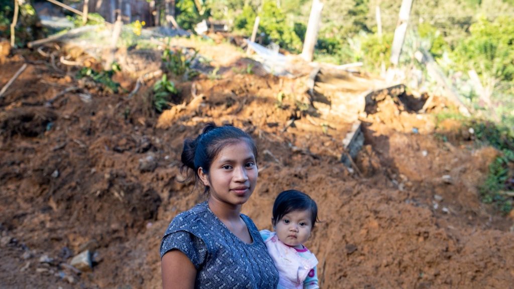 16 year old Lourdes López Vásquez_holding her baby in front of landslide damage in her village in Honduras