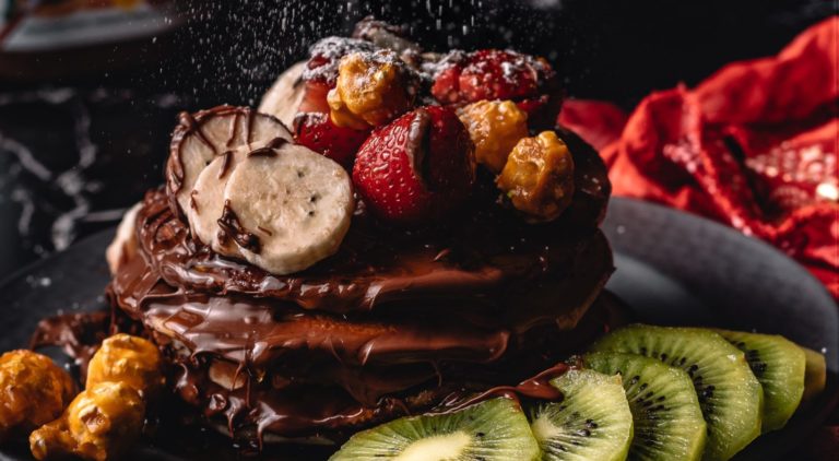 Chocolate pancakes stacked with chocolate sauce and fruit on top