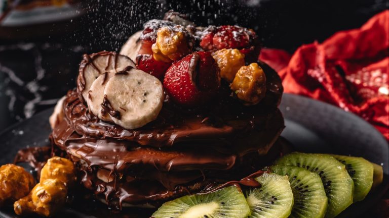 Chocolate pancakes stacked with chocolate sauce and fruit on top