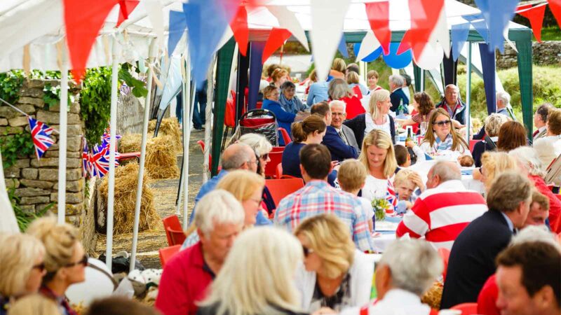 outdoor street party with bunting and people and children sitting celebrating at tables