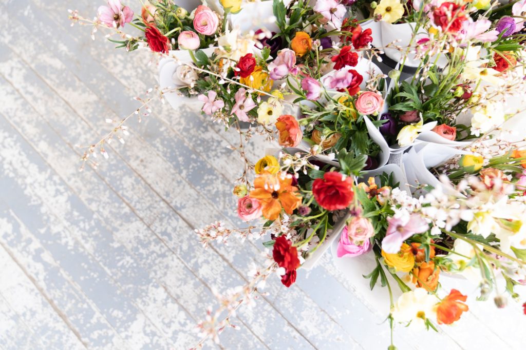 a white wooden table with a variety of flower bouquets in orange red and pink